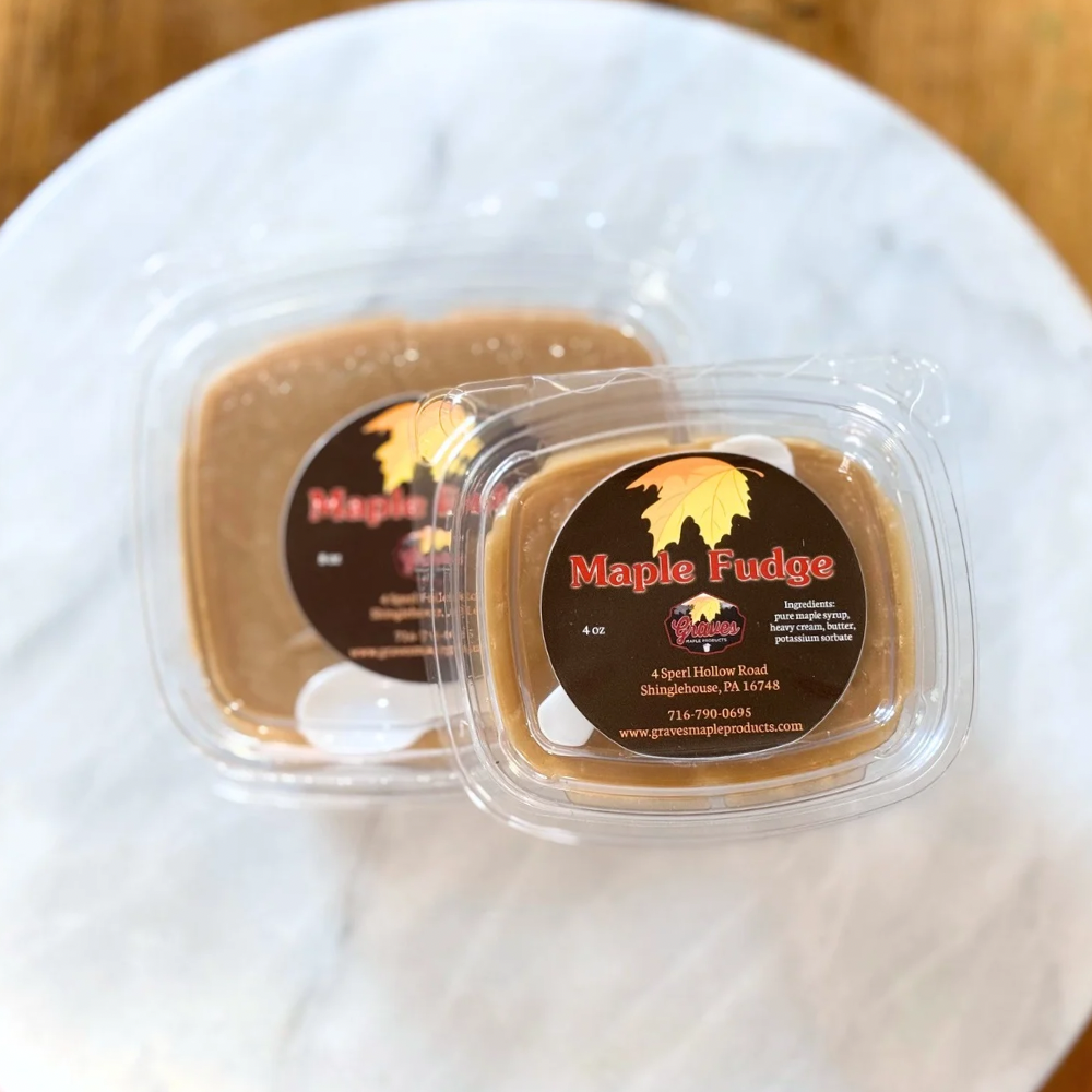 Two containers of maple fudge on a white plate with a wooden surface in the background.