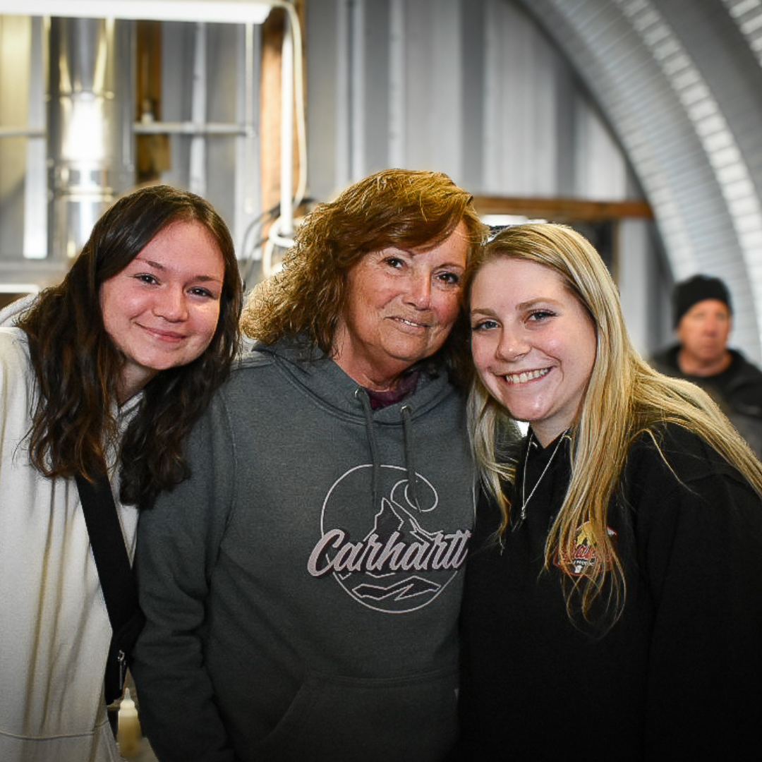 Graves Maple Products team members wearing Carhartt gear standing in front of stainless steel maple syrup equipment inside the sugarhouse during winter syrup production.